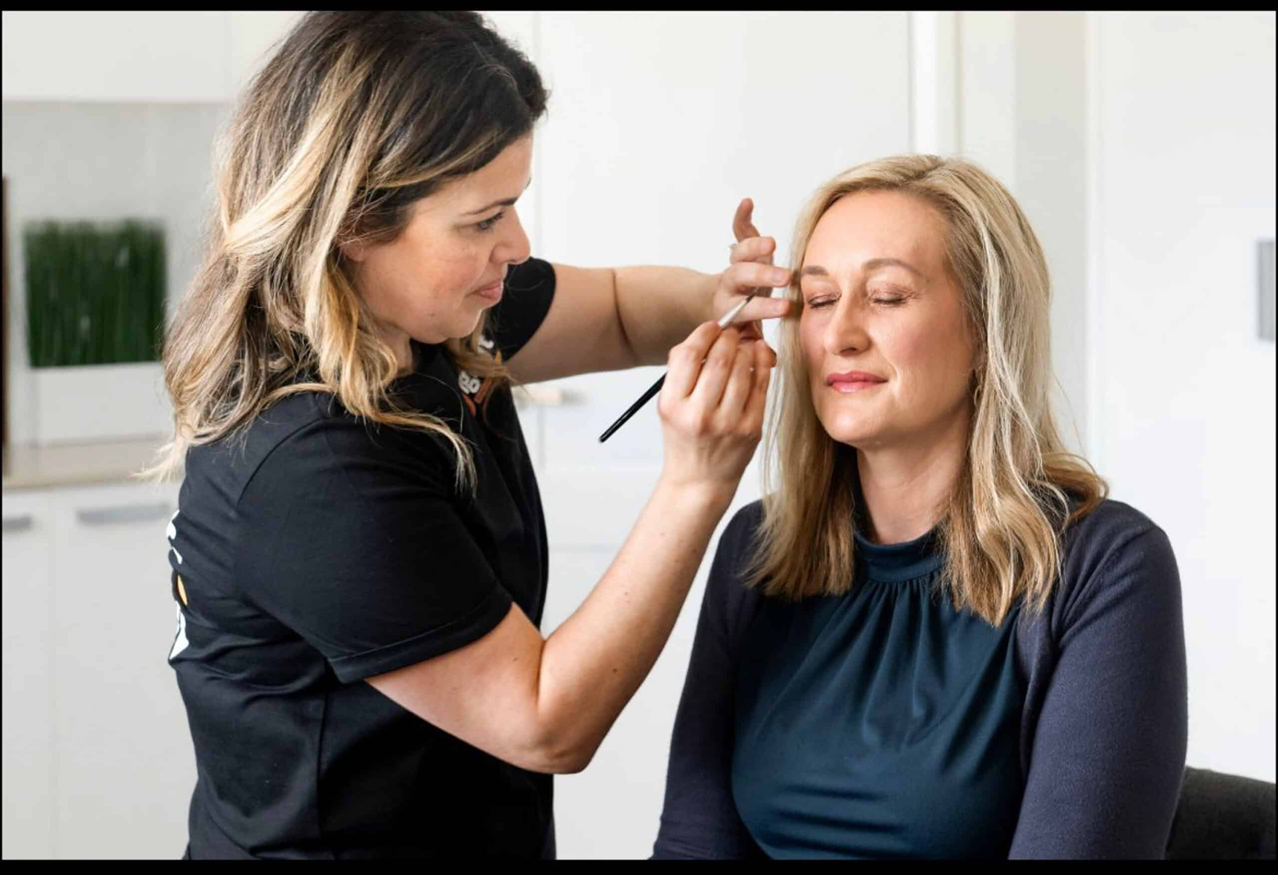 A makeup artist applies eye shadow to a lady s eyelid.