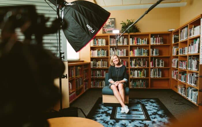 A lady is happily sitting in a library being interviewed during a half-day shoot by Concept Films.