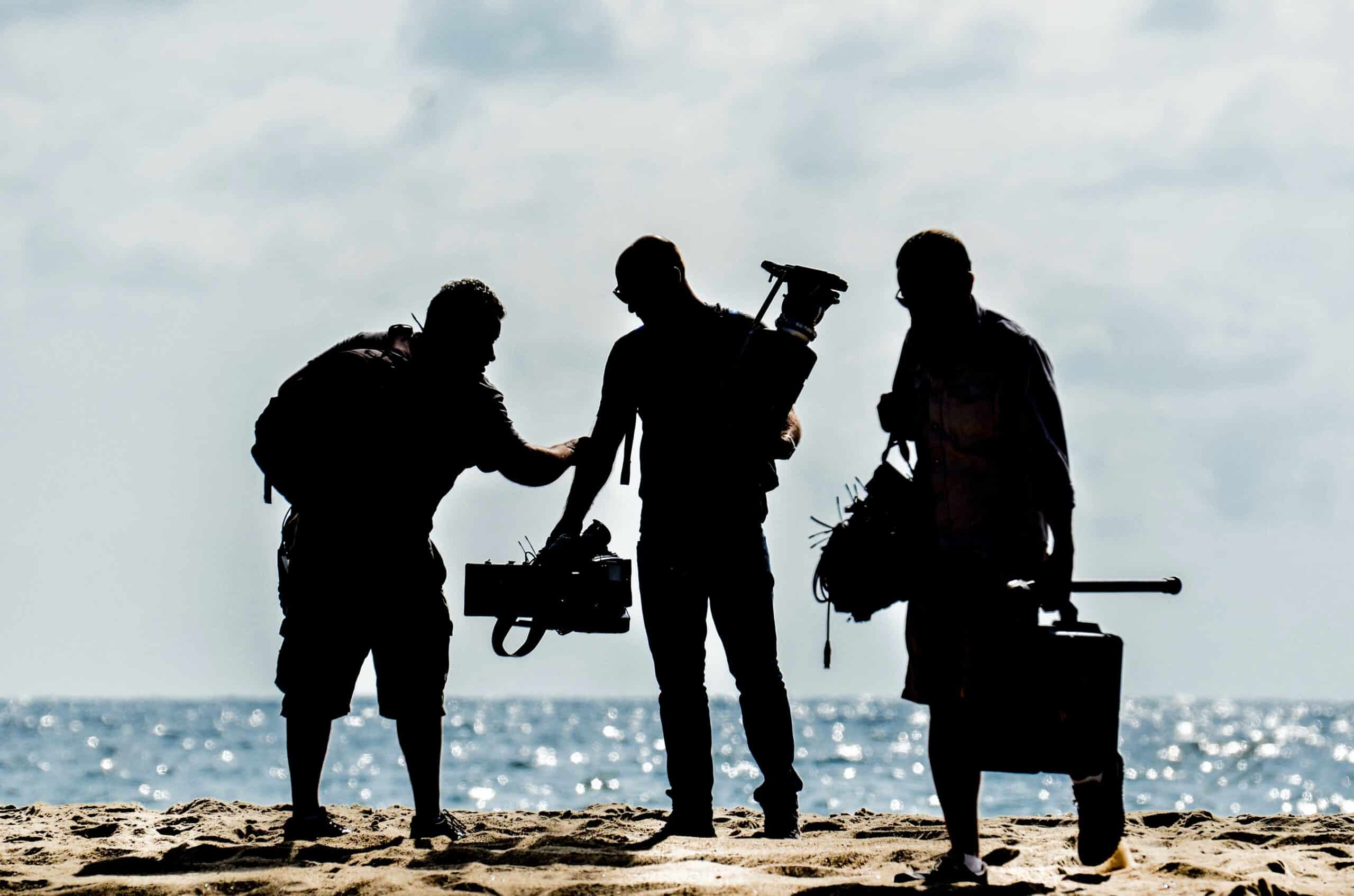 A team of three videographers from Concept Films carry video equipment on a beach during a full-day shoot.
